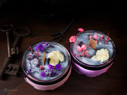 Candela votiva Ecate in cera argento-cenere con testa di dea scolpita, ametista grezza, fiori viola e rosa essiccati e stoppino di legno, accanto a chiavi antiche in ferro.