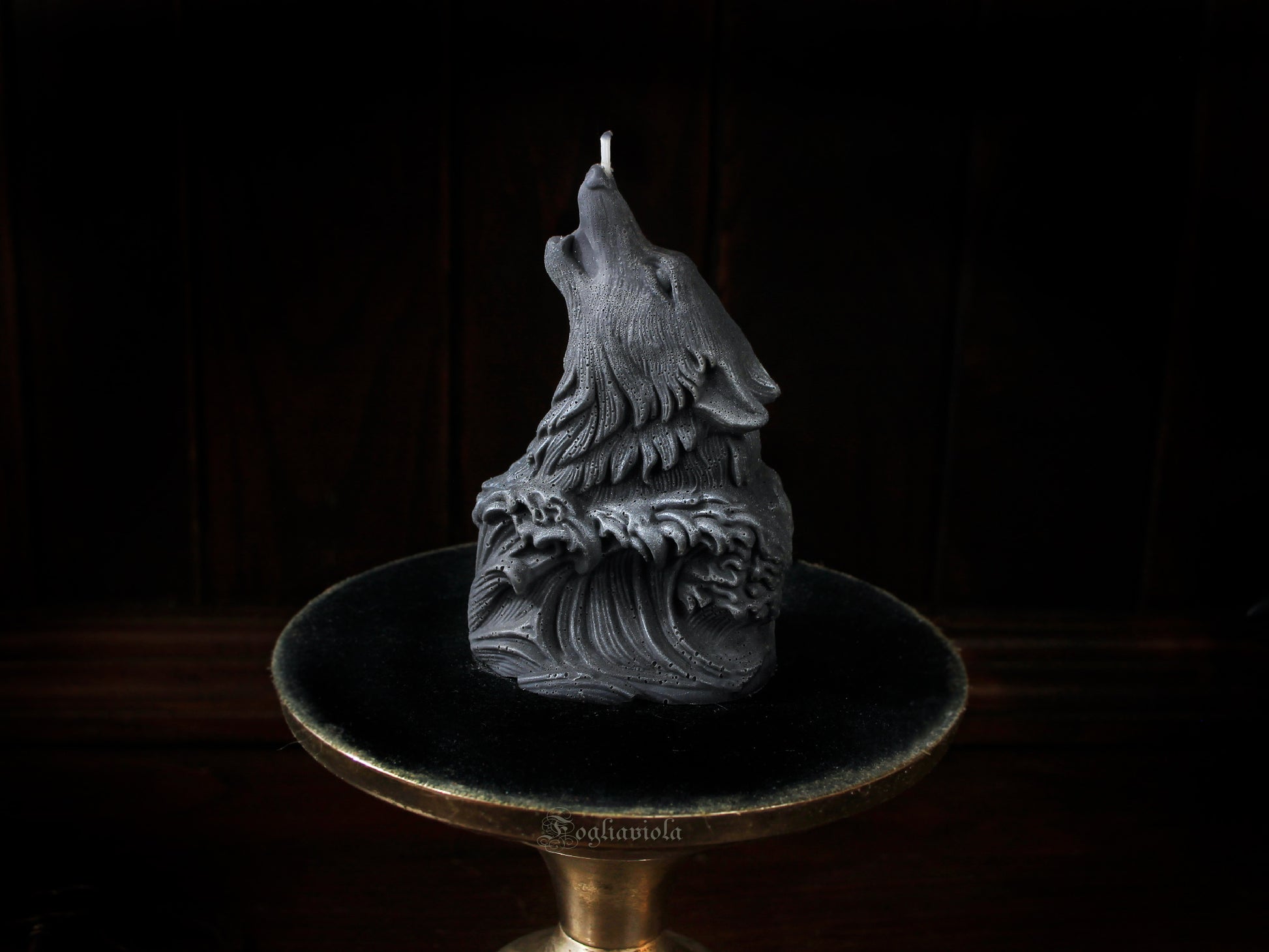 Candela scultura di un lupo grigio che ulula alla luna, emergente da un'onda scolpita, su alzata dorata e velluto nero — atelier Fogliaviola.